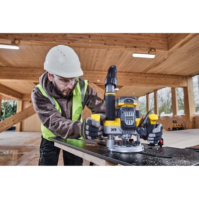 Håndværker med sikkerhedsudstyr bruger DeWalt 18V XR overfræser på træplade i et træbyggeri.
