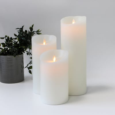 Sæt med tre hvide LED bloklys fra LEDlife med bevægelig flamme, arrangeret med en grå potteplante i baggrunden.