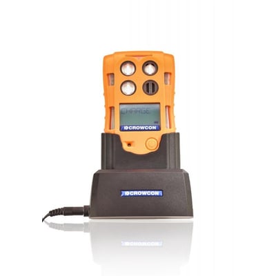 Crowcon T4 gasdetektor i sort bordlader med strømkabel, fotograferet med hvid baggrund og refleksion i overfladen.