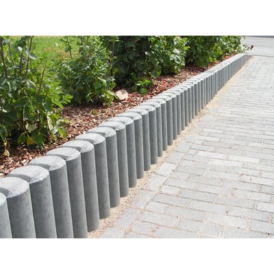 Grå hanit palisader i genbrugsplast, 11 x 80 cm, er monteret langs en græsplæne og et brolagt område.