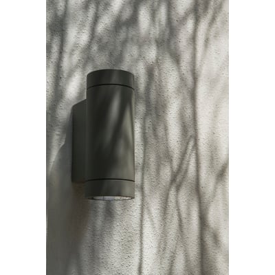 Astro 7586 Dartmouth Twin udendørs væglampe i sort, monteret på en lysgrå væg med skygger fra træer.