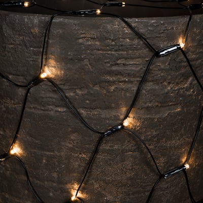 Tæt på Konstsmide Net lyskædens netstruktur med 250 varmhvide LED-lys mod en mørk, tekstureret baggrund.