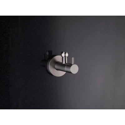 Vola S10-40 vinkelstopventil i børstet rustfrit stål, vist på en mørk, tekstureret væg.