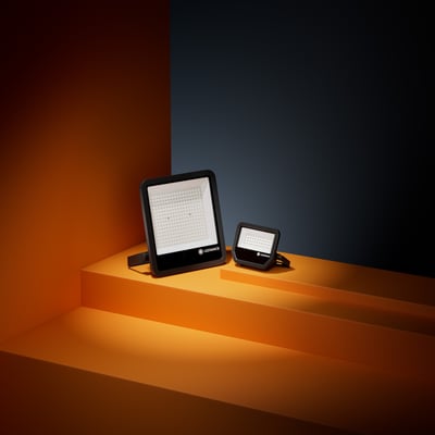 Sort LEDVANCE Floodlight Area Asym LED-projektør på orange podie, vist sammen med en mindre projektør.
