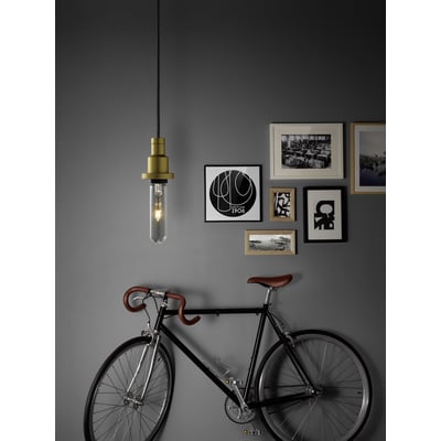 Ledvance 1906 tubular guld LED-pære hængende fra en fatning, med en cykel foran en billedvæg på en grå væg.