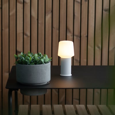 SACKit Base London hvid lampefod, der står på et sort havebord ved siden af en grå krukke med grønne planter.