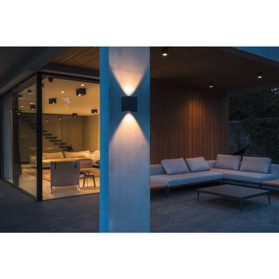 SLV MANA OUT udendørs væglampe monteret på en søjle med lysstråler op og ned, oplyser en terrasse med sofaer.