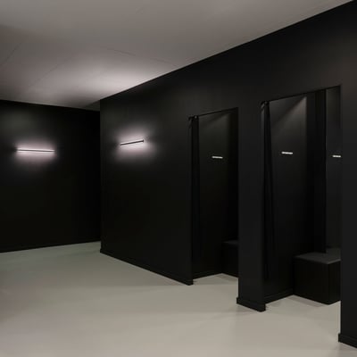 SLV ONE LINEAR 50 WL væglampe monteret på mørk væg i et rum med flere døråbninger og siddepladser.