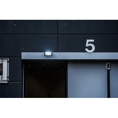Brennenstuhl 30W LED projektør monteret på en mørk bygningsfacade, lyser op i snevejr ved en port.
