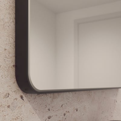 Nærbillede af hjørnet af Loevschall Refine spejlet med en tynd, sort metalramme og afrundede kanter.