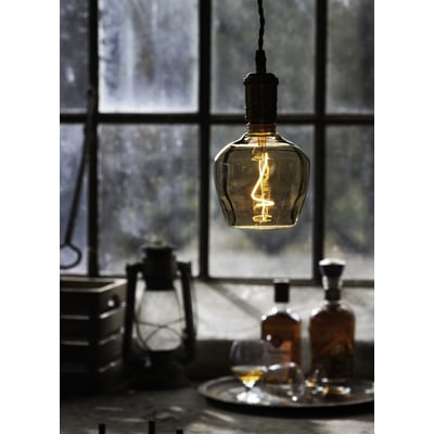 Brandy globe LED-pære med E27 fatning, 4W, 1800K, som hænger ned foran et vindue med flasker og et glas.