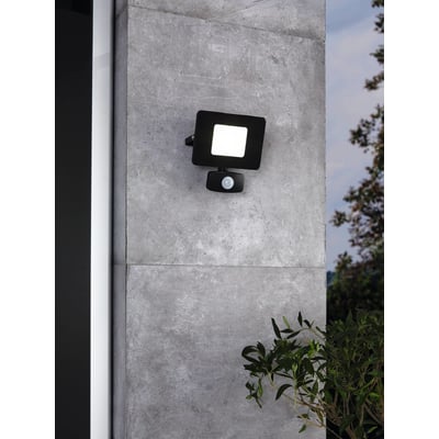 EGLO Faedo 3 udendørs væglampe i sort aluminium med integreret 20W LED og PIR bevægelsessensor, monteret på en grå stenmur med grønne planter i forgrunden.