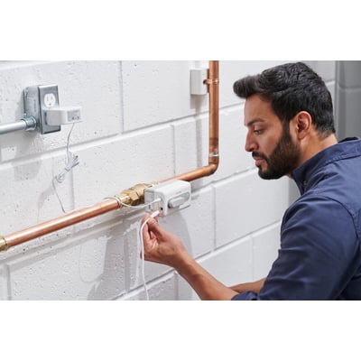 Resideo Braukmann L5 WiFi vandlækagestopventil monteret på kobberrør, mens en mand tilslutter strømkablet.