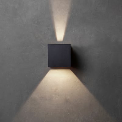 Sort Lumenlight Toscana udendørs væglampe med kantet form, monteret på grå væg og tændt med lys opad og nedad.
