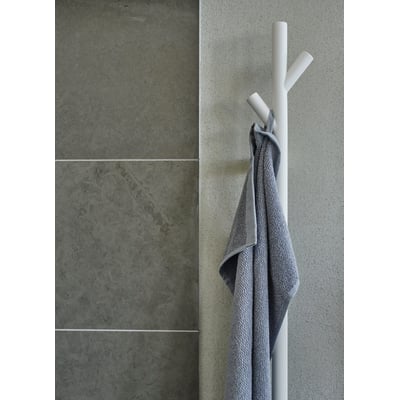 Smedbo dry håndklædetørrer i hvid mat med en gråmeleret håndklæde hængende på en af de tre arme, monteret på en betonlignende væg.