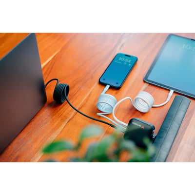 Verbatim Sync & Charge USB-C-kabel i blå ligger oprullet på et træbord ved siden af en telefon og tablet.