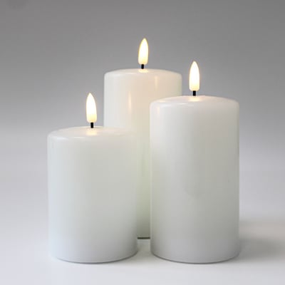 Tre hvide LED-bloklys med realistisk flammeeffekt, vist fra siden mod en hvid baggrund, alle lysene er tændte.