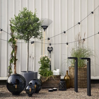 Star Trading Small Circus lyskæde spændt ud over en have med møbler og planter, viser udendørs anvendelse.