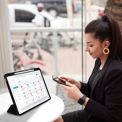 4smarts Folio Case Basic til iPad Pro 11" (M4/M5) i sort PU-læder, demonstreret med en kvinde, der bruger den på en cafe.