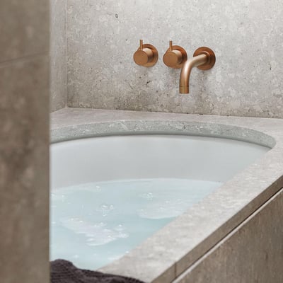 Vola 2-grebsblander med keramiske ventiler i messingfarve monteret over et badekar med vand.