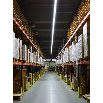 Langt LEDVANCE TruSys Flex armatur monteret i et lager med reoler fyldt med varer, og oplyser midtergangen med et bredt hvidt lys.