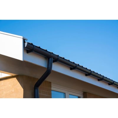 Plastmo gråt nedløbsrør på 75mm monteret på husets facade med klar blå himmel i baggrunden.