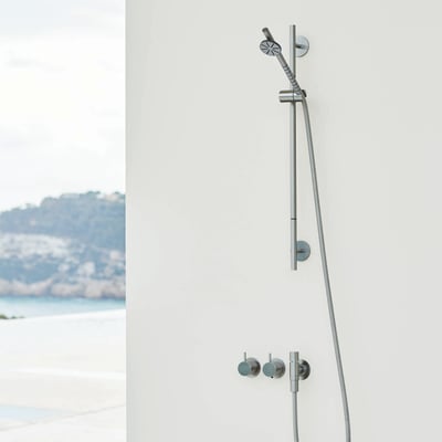 Vola indbygningstermostat med fast afgangsmuffe T60 og håndbruser på en hvid væg, med udsigt til hav og kystlinje i baggrunden.