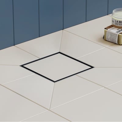 Hansgrohe afløbsskål i børstet rustfrit stål med en ramme på 100 x 100 mm, monteret i et cremefarvet flisegulv med mørkeblå vægpaneler bagved.