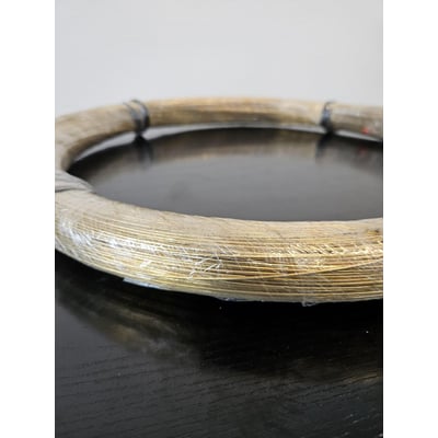 Spole af massiv messingtråd på 1.5 mm og 2 kg, indpakket i klar plast på mørkt bord.