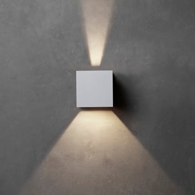 Hvid Lumenlight Toscana udendørs væglampe med up- og downlys monteret på en mørk væg.