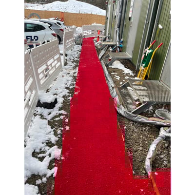 Rød spaghettimåtte på 1x15 meter, lagt ud på en grusvej foran en bygning med sne i omgivelserne.