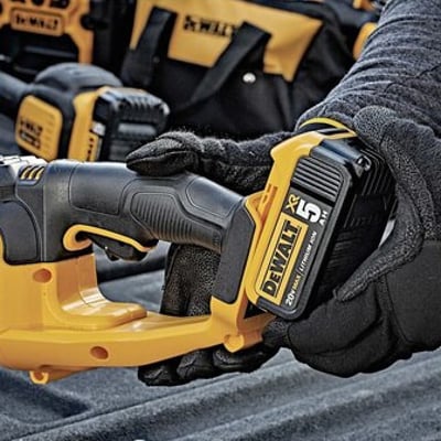 Hænder i arbejdshandsker monterer et DeWalt 18V XR batteri i den gule hækkeklipper.
