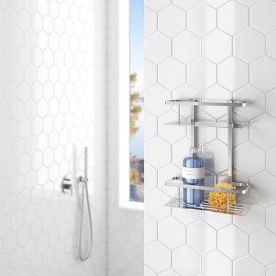 Smedbo Sideline dobbelt brusekurv i poleret krom, monteret på et hvidt sekskantet flisevæg ved siden af et brusehoved og et vindue.