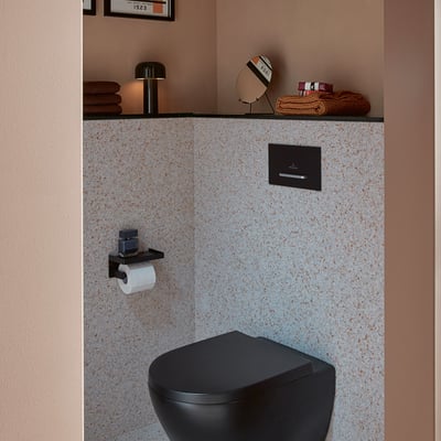 Villeroy & Boch ViConnect E300 betjeningsplade i mat sort med kromknap, monteret over et sort toilet.