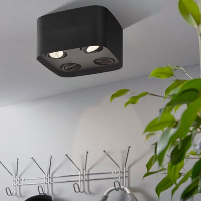 Sort EGLO Caminales-Z påbygningsspot med fire lyskilder monteret på et hvidt loft ved siden af en plante og en knagevæg.