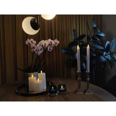 Hyggelig atmosfære med Veli Line 3D T-lys, orkidé og grøn plante i et rum med gyldne gardiner.