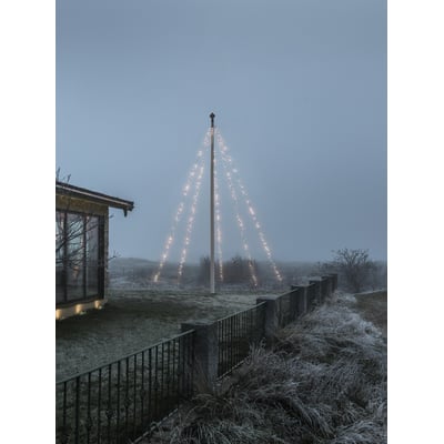Konstsmide flagstangskæde med 500 LED-lys, monteret på en flagstang ved et hus i tusmørke.