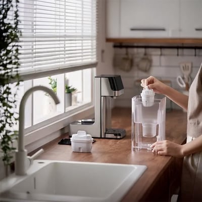 Philips vandautomat ADD5910M/10 med 2,2L kapacitet placeret på køkkenbordet ved vinduet, mens en hånd fylder vand i.