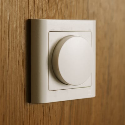 Niko DALI-2 lysdæmper i hvidt, dansk design, monteret på en trævæg med en rund drejeknap for lysjustering.