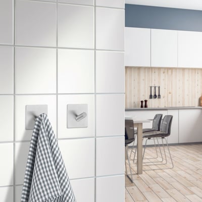 Smedbo Beslagsboden selvklæbende enkelkrog i børstet stål, 45 mm, monteret på hvidt badeværelsesflise, med et ternet viskestykke hængende.