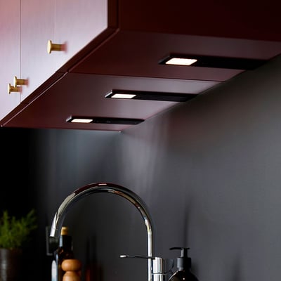 Loevschall Stella spot kit med 3 sorte spots monteret under et mørkerødt overskab over en køkkenvask.