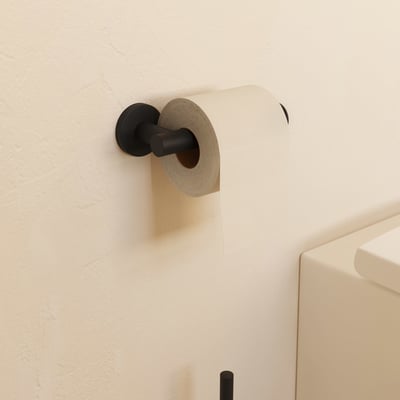 Cosmic Architect S+ toiletpapirholder i mat sort, monteret på en lys væg med en rulle toiletpapir påsat.
