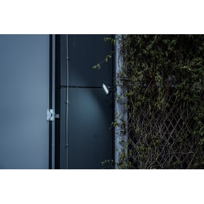 Brennenstuhl LED projektør 100W, der lyser på en mørk facade, fremhæver projektørens kraftige lys og 6500K hvide lysfarve.