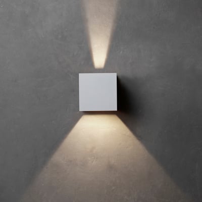 Hvid Lumenlight Toscana væglampe med up- og downlight monteret på en grå væg.