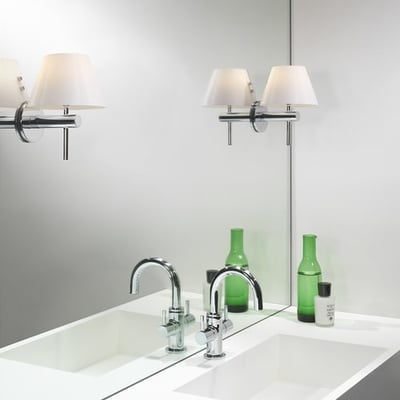 Astro Roma væglampe i krom med opal glasskærm, monteret over et hvidt badeværelsesmøbel med vaske og grønne flasker.