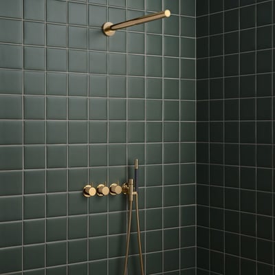 Vola indbygningstermostat med omskifter og håndbruser i guld monteret på mørkegrønne badeværelsesfliser.