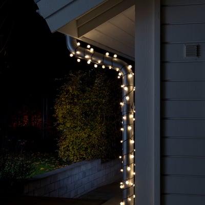 Konstsmide lyskæde med 80 varmhvide LED'er monteret på et tagrende ved en hvid træbeklædt væg om natten.