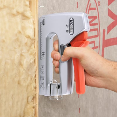 Tacwise Z4-140 klamme- og stift pistol i brug på isolering og dampspærre, med hånd der betjener håndtaget.