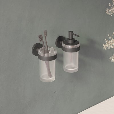 Cosmic tandkrus i mat sort, vist ved siden af en sæbedispenser på en grå væg med planter.