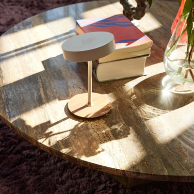 Halo Design On the move batteri bordlampe i hvid metal placeret på et marmorbord med bøger ved siden af. Den har en rund lampehoved og en elegant stander.